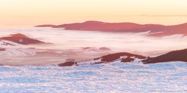 Eastern Sudetes, view of mountain range with thick fog in valley from peak from hiking trail during winter hike in mountains, viewpoint of wide winter landscape in mountains at orange sunset. clipart