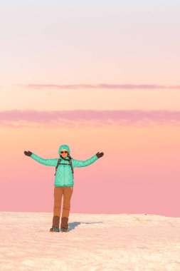 Eastern Sudetes, Young woman hikes on mountain snow-covered trail, stands on mountain top and shows colorful sky at sunset, winter landscape in mountains. clipart