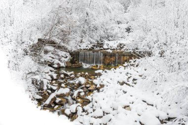Kışın dağ nehri, karla kaplı kayaların üzerinden nehir yatağından aşağı akar. Kış manzarası bir dağ yürüyüşü patikasında.
