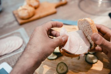 Erkek eller jambonlu ve sebzeli sandviç yapıyor, manzarayı kapat. Adam mutfakta atıştırmalık hazırlıyor.