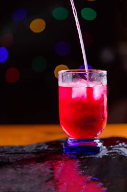 Pembe ferahlatıcı içecek, buzlu, mavi renkli ve arka planda odandan çıkarılmış ışıklar. Düşük alkollü lolipop likörü