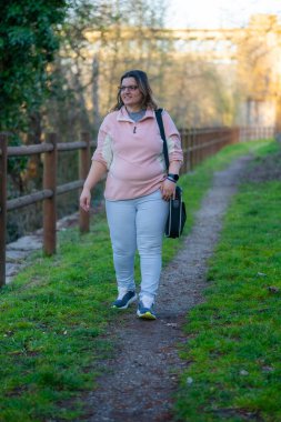 Dışarıdan giyinen bir kadın bilgisayarını saklamak için rahat ve rahat bir şekilde bir çanta taşıyor çünkü aynı zamanda dijital dünyaya bağlı.