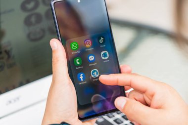 Lugo, İspanya - 05 Eylül 2023: Sosyal uygulamaları ekranda ve dizüstü bilgisayarında olan akıllı telefonu tutan kadın. Ekranda ve laptopta sosyal medya simgeleri var. Sosyal ağlar en popüler araçtır. Akıllı telefon yaşam tarzı. Sosyal medya uygulaması başlatılıyor