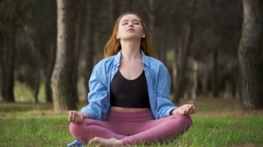 Kızıl saçlı genç kadın ormanda meditasyon yapıyor. Doğada meditasyon.