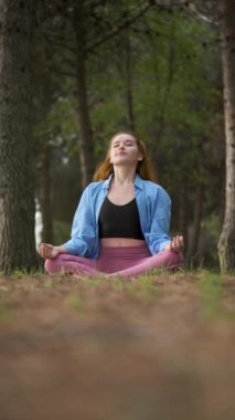 Kızıl saçlı genç kadın ormanda meditasyon yapıyor. Doğada meditasyon.
