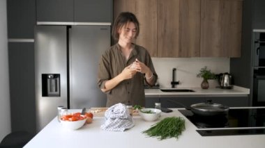 Gülümseyen Asyalı genç adam yemek tariflerini kontrol ediyor ve mutfakta fotoğraf çekiyor..