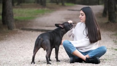 Kafkasyalı genç bir kadın Amerikan Stadyumu ve Fransız Bulldog 'una çam ormanında otururken onunla nasıl nazikçe oynayacağını öğretiyor..
