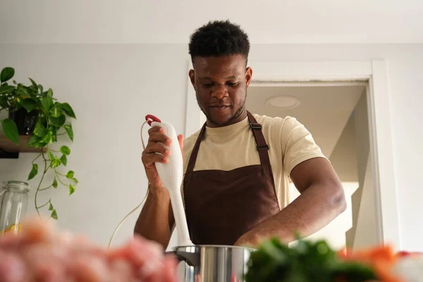 stock image Young african man using a blender to prepare chicken mince in a kitchen.