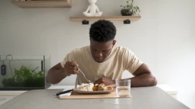 Genç siyah adam oturma odasında kızarmış tavuk, pirinç ve domates soslu muz yiyor..