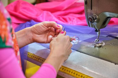 Tanımlanamayan terzi dikiş atölyesinde ipliği dikiş makinesine kesiyor.