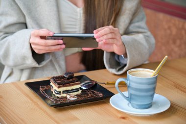 Kafede yemeden önce akıllı telefonuyla pastanın fotoğrafını çeken tanınmamış bir kadın..