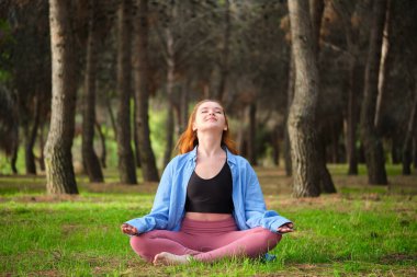 Kızıl saçlı genç kadın ormanda meditasyon yapıyor. Doğada meditasyon.