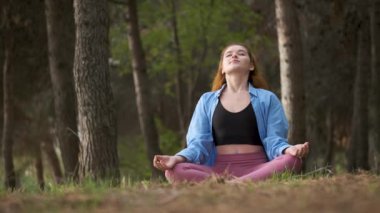 Kızıl saçlı genç kadın ormanda meditasyon yapıyor. Doğada meditasyon.