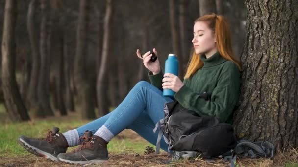 Wędrowna Ruda Kobieta Wyciąga Butelkę Wody Plecaka Pije Pod Drzewem — Wideo stockowe