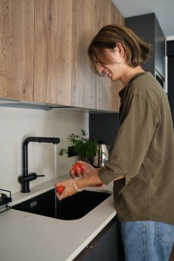 Gülümseyen Asyalı genç adam lavaboda taze domatesleri duruluyor..