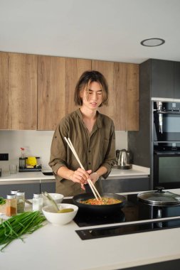 Gülümseyen Asyalı genç adam Çin veya Tayvan domatesi pişirirken mutfakta çırpılmış yumurta pişiriyor..