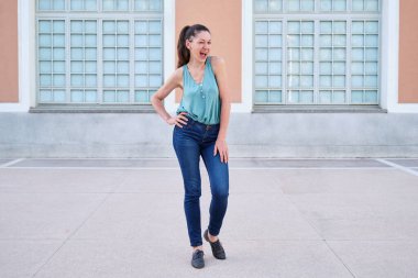 Bir kadının göz kırparken, gülümserken ve caddede kameraya bakarken tam boy görüntüsü..