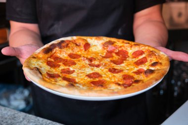 Şefin elleri taze pişmiş pepperonili pizzayı tutuyor. Pizzacı..
