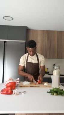 Genç siyah adam mutfakta tavuk tarifi hazırlamak için kırmızı biber kesiyor..