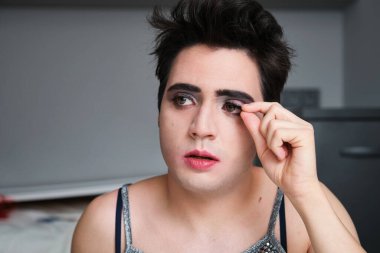 Genç travesti siyah kirpiklerini çıkarıyor..