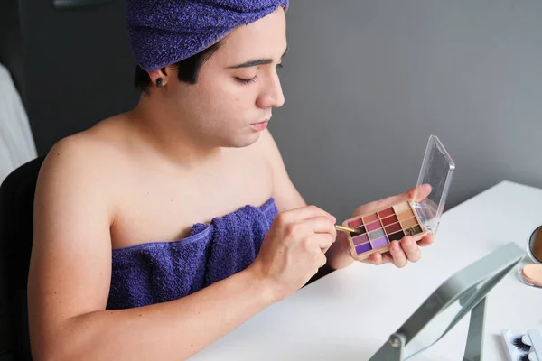 Young transgender man choosing the right color of eyeshadow from a case.