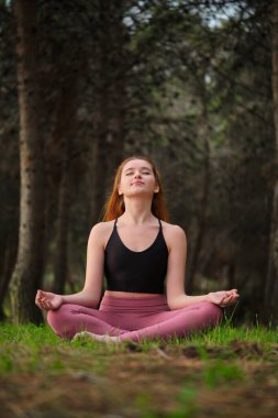 Kızıl saçlı genç kadın ormanda meditasyon yapıyor. Doğada meditasyon.