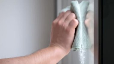 Close up of man hands cleaning window with cloth and spray. Household chores.