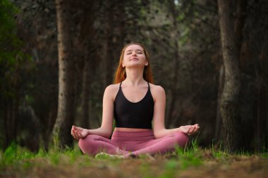 Kızıl saçlı genç kadın ormanda meditasyon yapıyor. Doğada meditasyon.