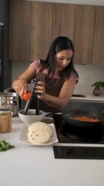 Genç Venezuelalı kadın mutfakta arepaları hazırlamak için domates rendeliyor..