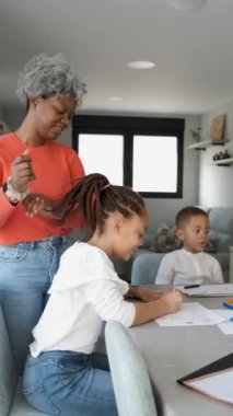 African mother doing a ponytail to her daughter braided hair while she and her brother are painting.