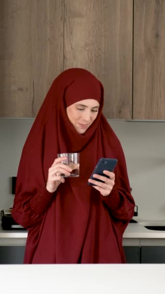 Muslim Young Woman Hijab Drinking Water Using Smartphone Kitchen Home — Stockvideo