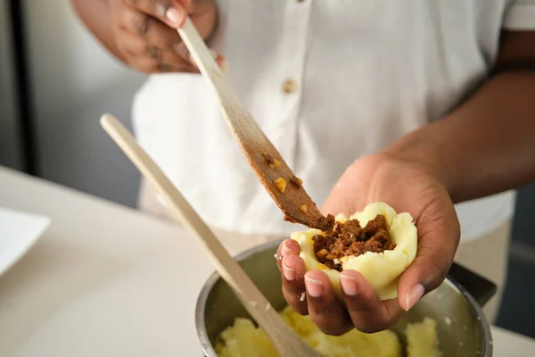 Close up of cuban woman hands filling mashed potatoes with minced beef to prepare cuban style stuffed potatoes.