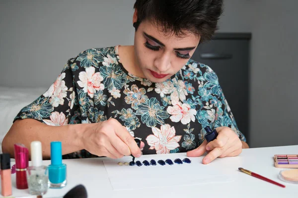 Young gender fluid person in a dress painting false nails.