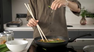 Close up of asian young man hands adding chive to prepare chinese or taiwanese tomato scrambled eggs at kitchen.