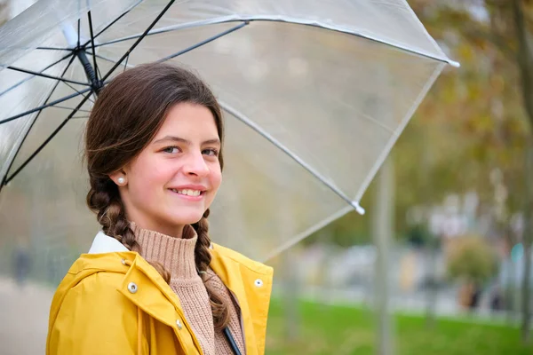 Portrait of preteen girl in yellow raincoat and umbrella smiling and looking at camera outdoors in autumn.