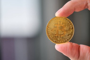 Hand holding a golden Bitcoin coin token. Cryptocurrency, finance and business concept.