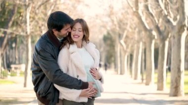 Happy pregnant couple embracing and touching her belly looking each other in a park. Pregnancy.