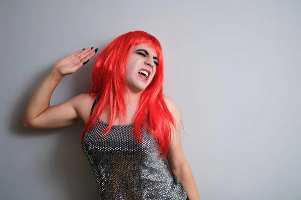 Portrait of gender fluid male screaming and wearing a red wig on grey background. LGBTQ queer.