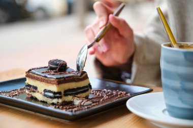 Unrecognizable woman eating a cake and drinking coffee in a cafeteria.
