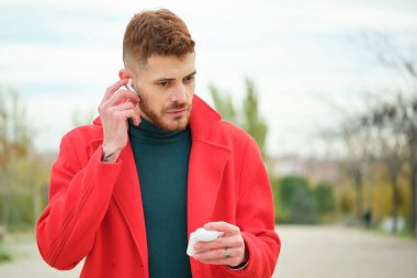 Sonbaharda sokakta kablosuz kulaklık takan kırmızı ceketli Latin bir gencin portresi..