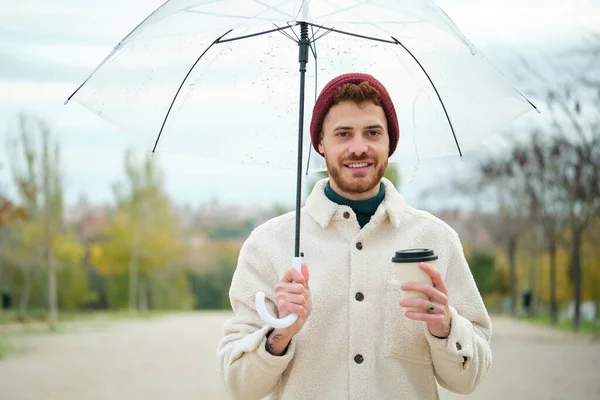 stock image Young man with a coffee and transparent umbrella in street in winter.