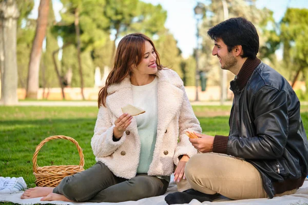 若いカップルがお互いを見て 公園のピクニックでサンドイッチを食べる — ストック写真
