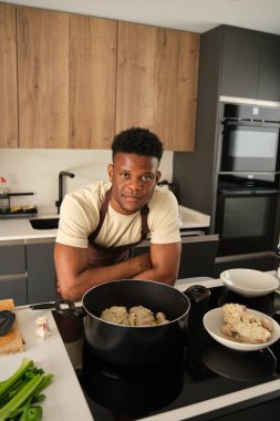Genç siyah adam gülümseyip kameraya bakarken mutfakta sebze tarifli kızarmış tavuk kıyması hazırlıyor..