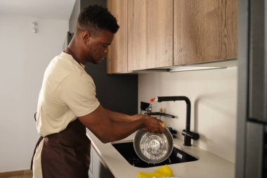 Genç Afrikalı bir adam mutfakta paslanmaz çelik tencereyi sabunla yıkıyor..