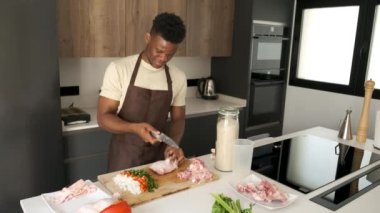Genç Afrikalı bir adam mutfakta yemek tarifi hazırlamak için tavuğun derisini yüzüyor..
