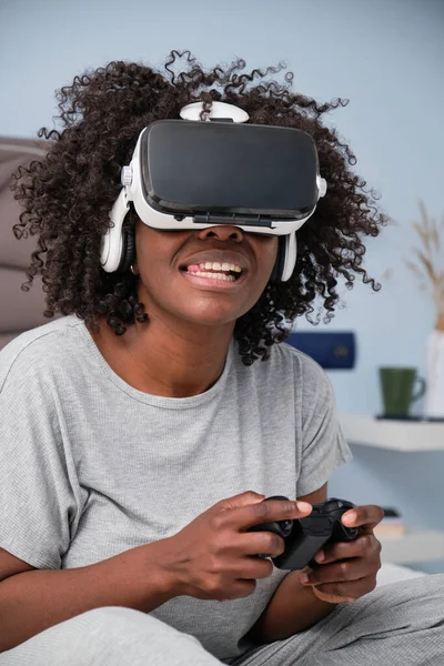 Young black woman plays video games with VR headset on bed in the morning.