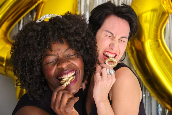 两个多种族的快乐女人在一个40岁生日聚会上咬着40岁生日的金色蜡烛 — 图库照片
