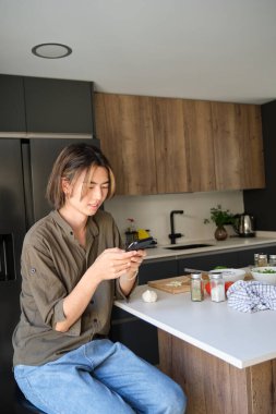 Smiling asian young man checking recipe on mobile phone at kitchen.