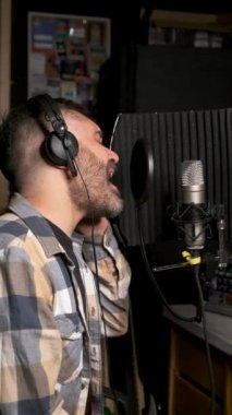 Kulaklık takan erkek şarkıcı mikrofonlu yeni bir single 'ı bir müzik stüdyosunda kaydediyor..