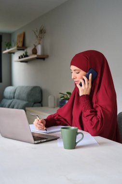 Evde dizüstü bilgisayarda çalışırken tesettürlü genç Müslüman bir kadın..